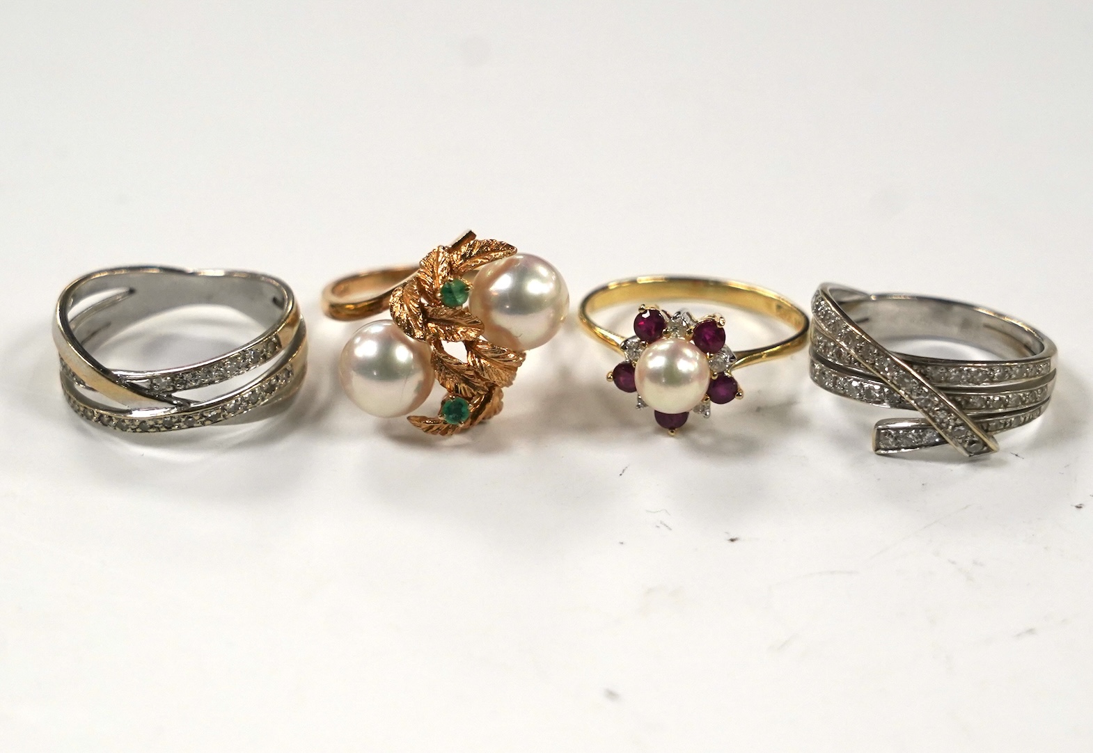 Two modern continental yellow metal and diamond chip set triple band cross over rings, size N, a 14k, ruby, diamond and cultured pearl set cluster ring, a 14k, two stone cultured pearl and a two stone emerald set ring.